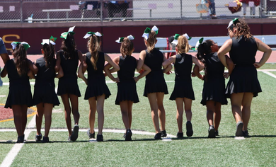 Cheerleader in red uniform performs a backbend on a green and red football field.