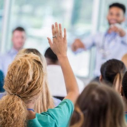 Unrecognizable female nurse raises hand to ask a question during medical conference. The conference speaker is pointing at her.
