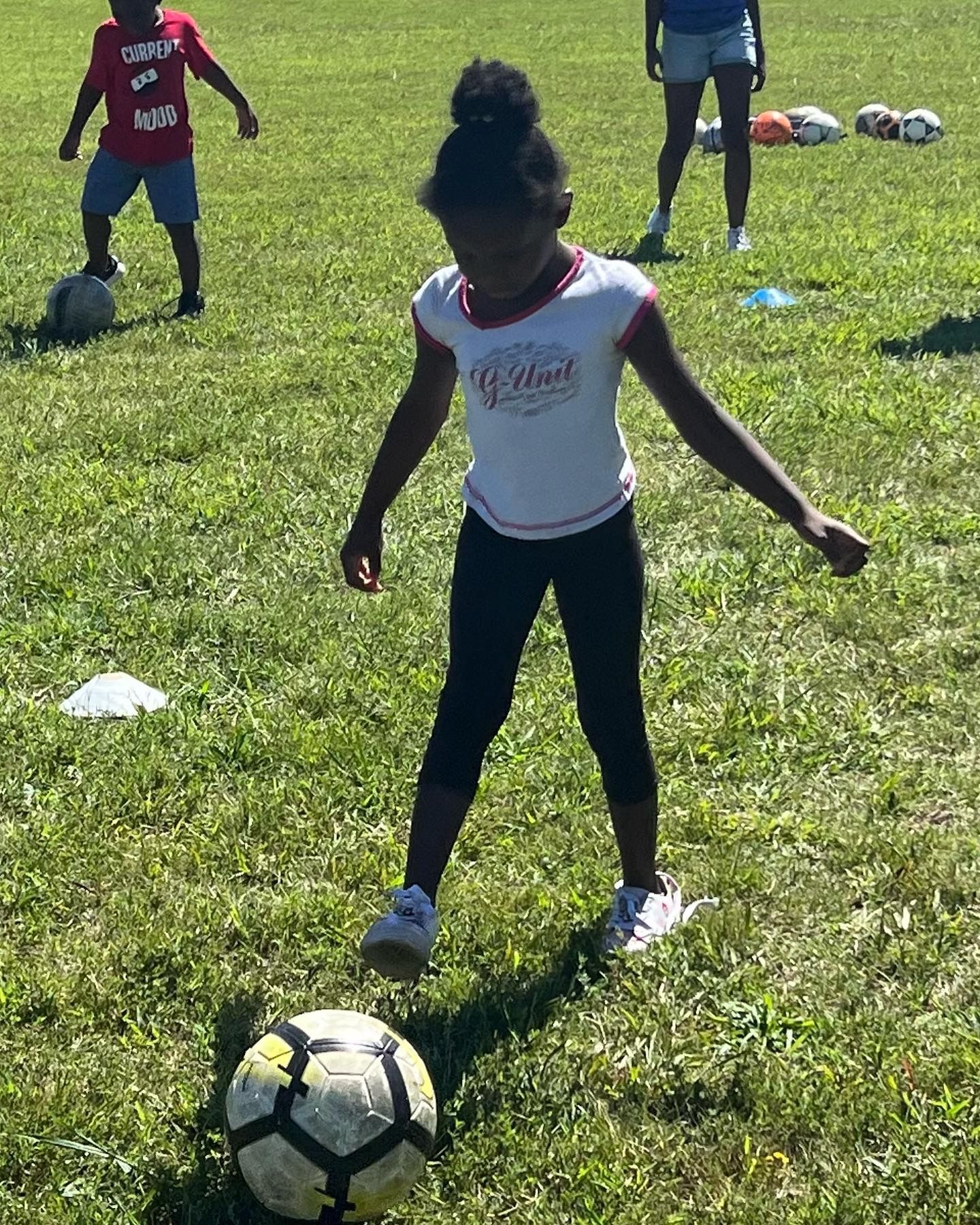 Child standing over a soccer ball on a grassy field during practice