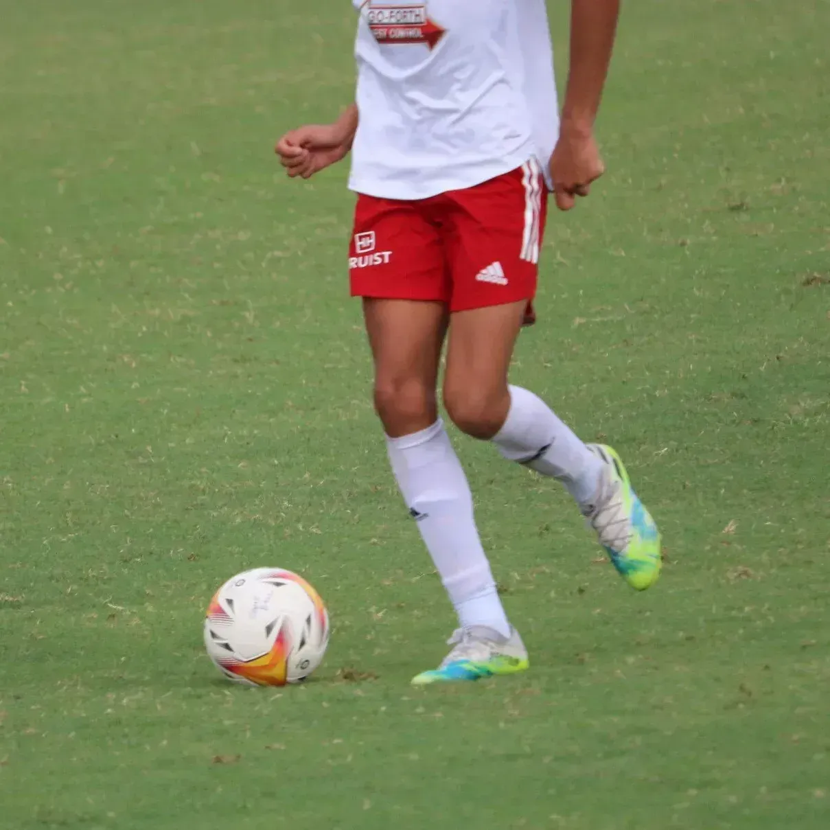 Soccer player in red shorts and white socks dribbling a ball on a grass field