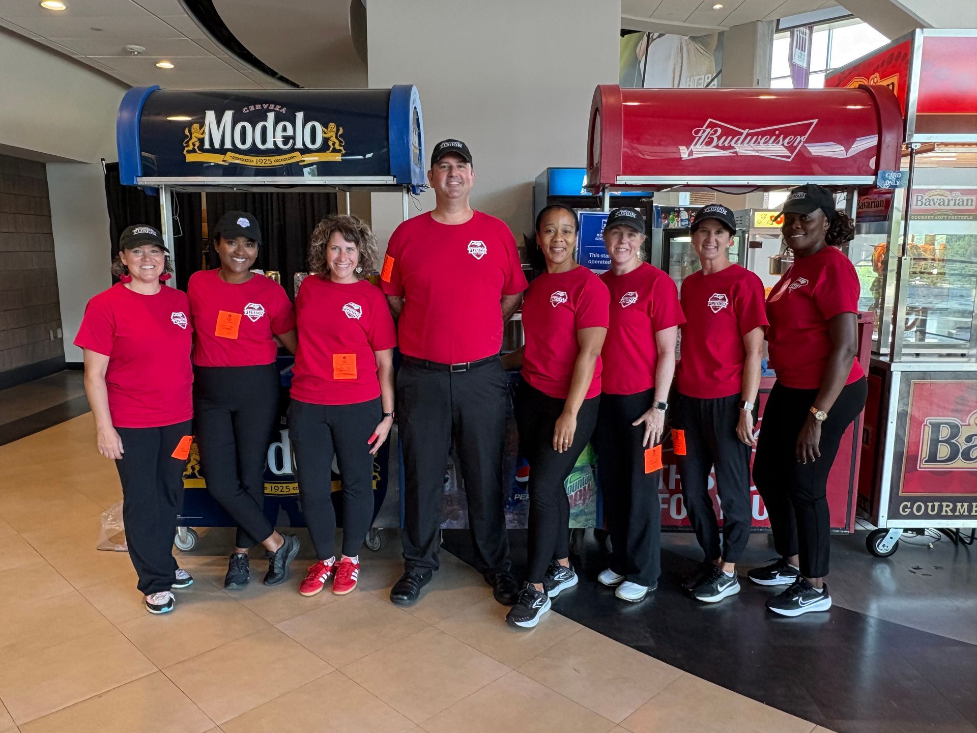 Group of people in red shirts posing indoors in front of Modelo and Coca-Cola coolers