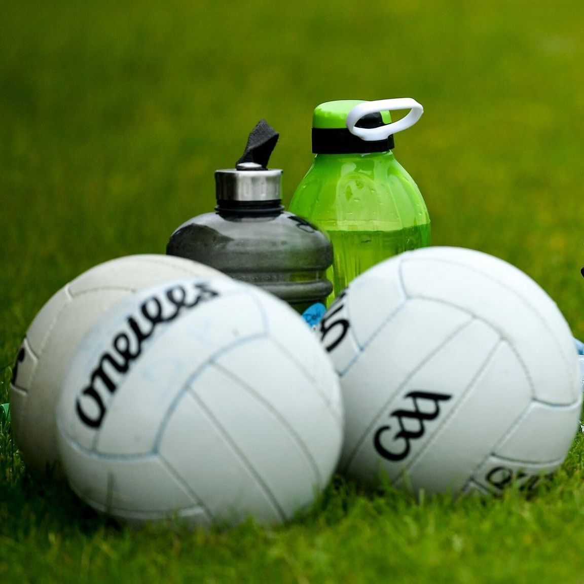 Two white volleyballs on grass with water bottles in the background
