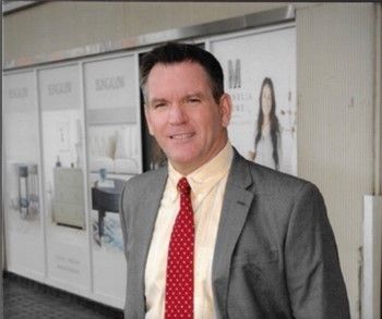 Man in gray suit and red tie standing in a hallway outside office displays