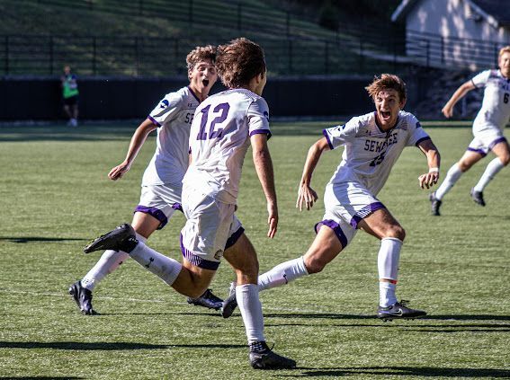 Soccer players in white uniforms chasing the ball on a sunny grass field
