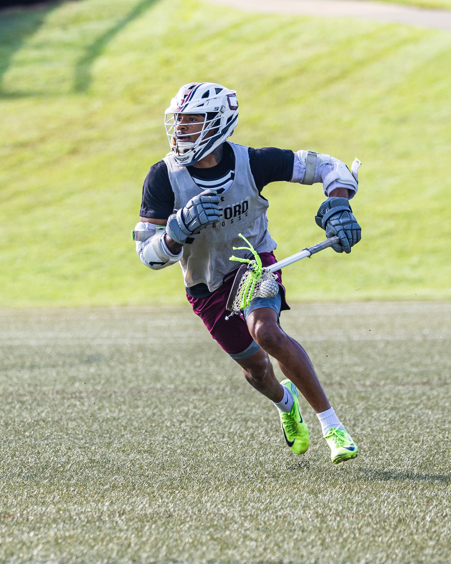 Lacrosse player in helmet and dark uniform running on grass field, holding a lacrosse stick.