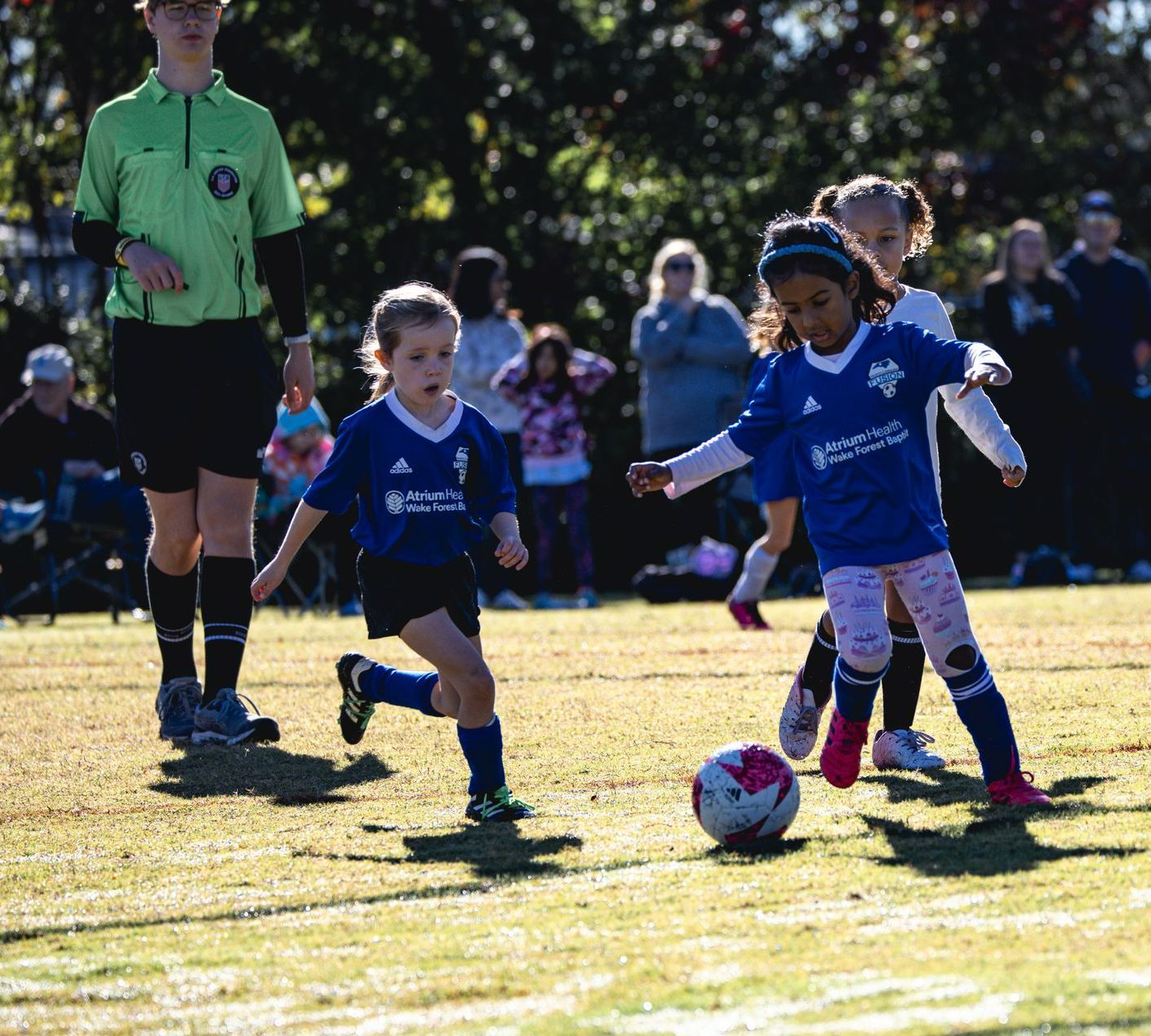 Youth soccer game with children in blue jerseys chasing the ball on a sunny field