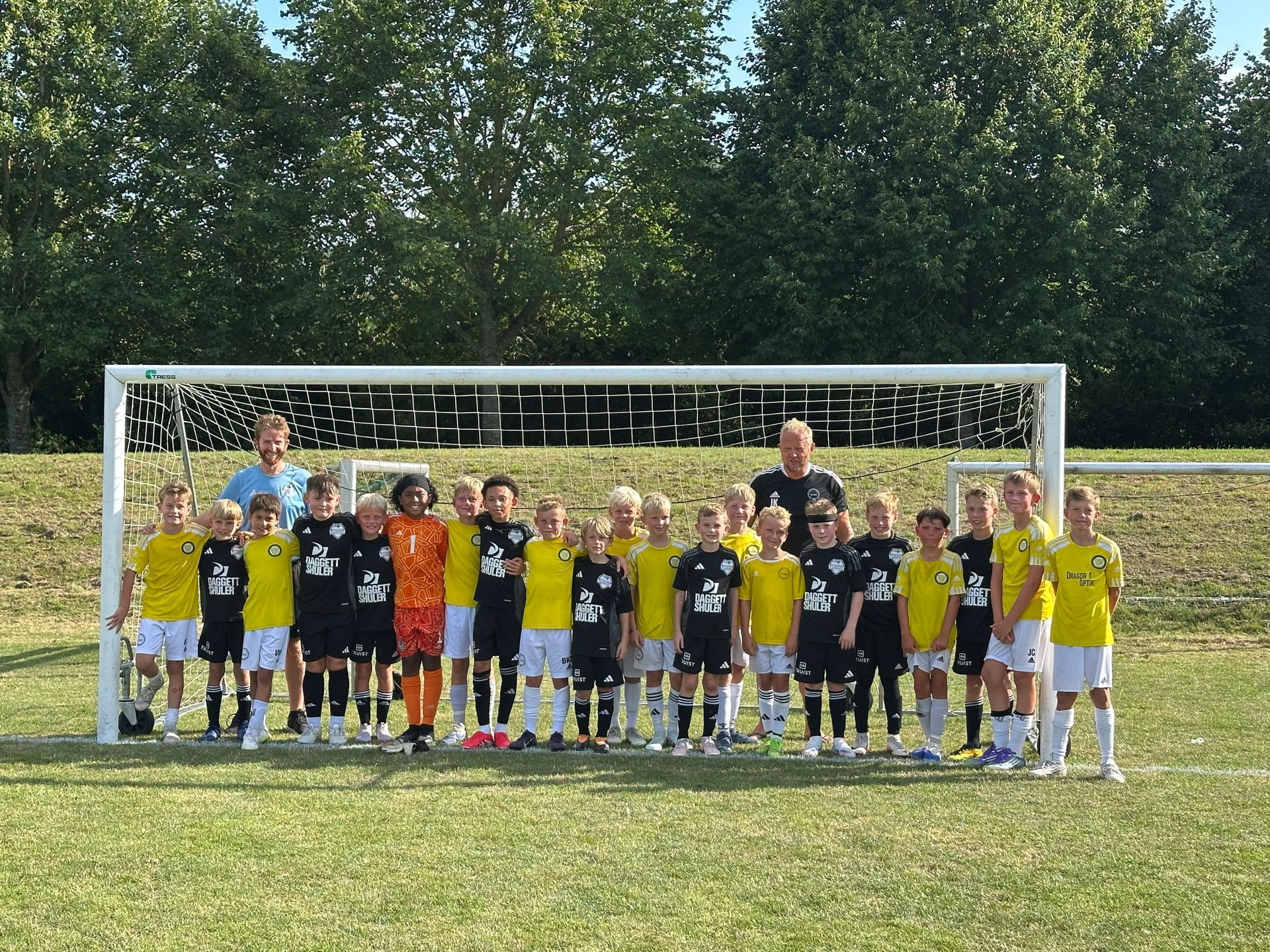 Youth soccer team posing in front of a goal on a grassy field, with coaches behind them.