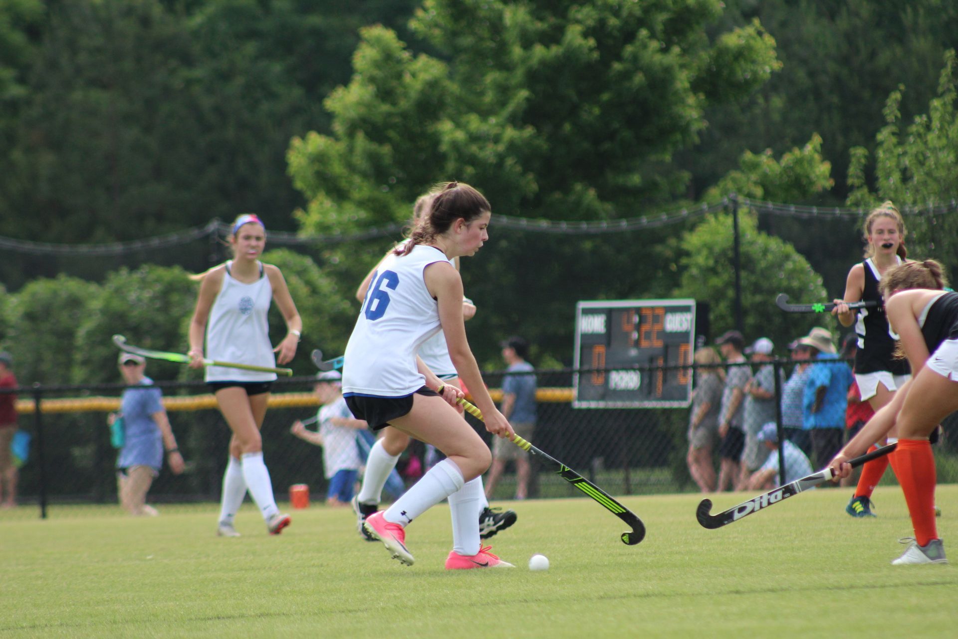 Field hockey players in white and orange compete on a grassy field during a match