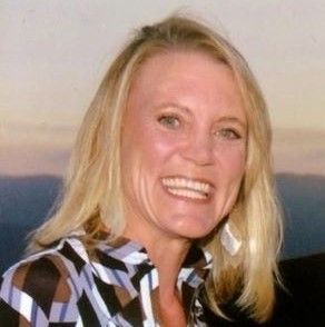 Smiling blonde woman in a black-and-white striped shirt against an outdoor sunset background