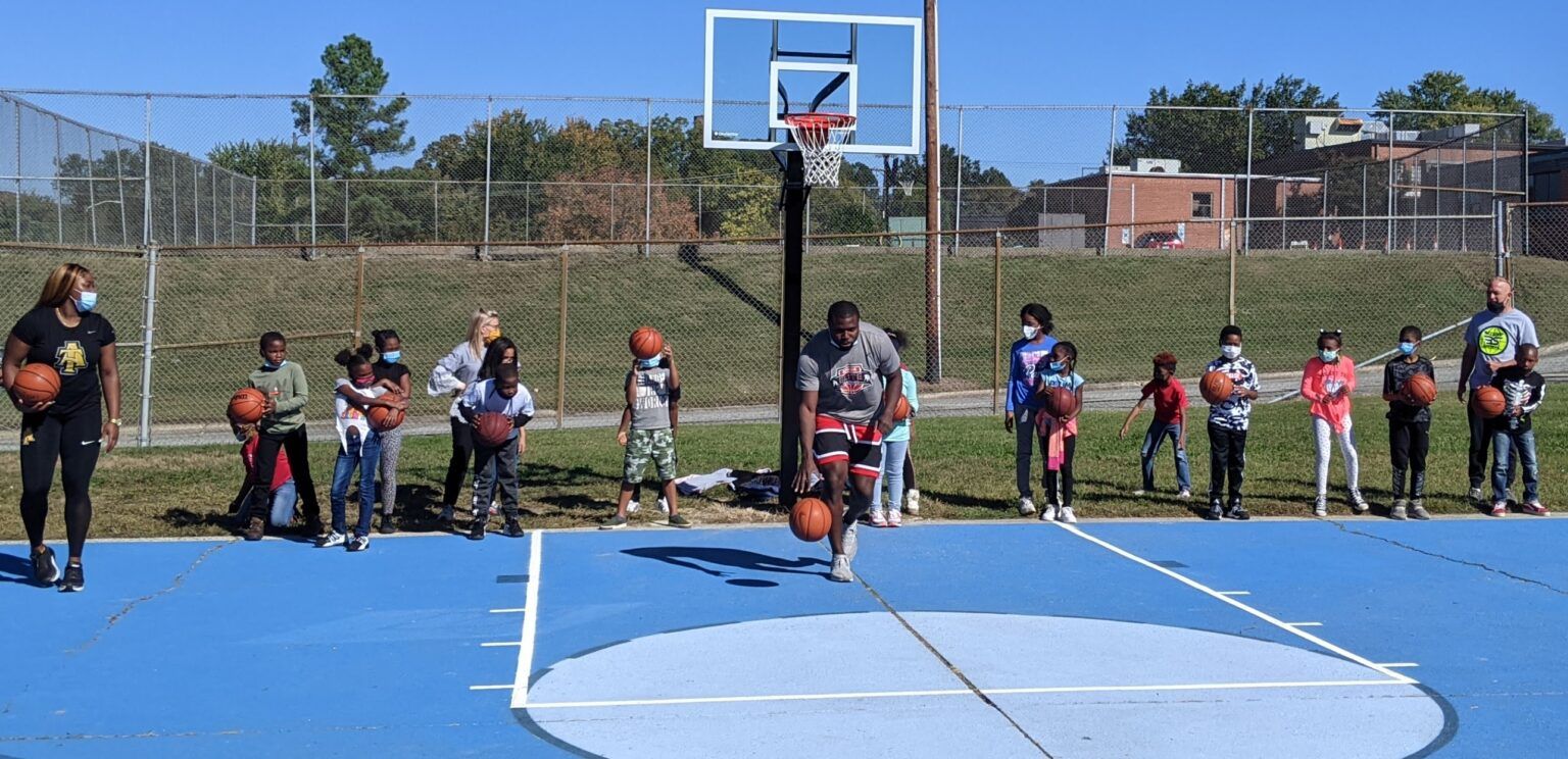 Basketball court with a player shooting free throws while spectators line the baseline.