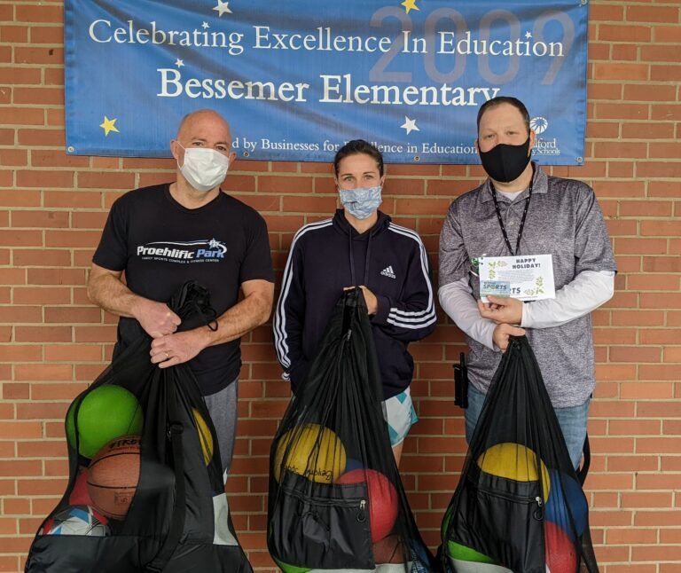 Three masked people hold black recycling bags in front of a Bessener Elementary banner.