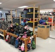 Thrift store aisle with shelves and racks of colorful shoes and boots under bright fluorescent lights