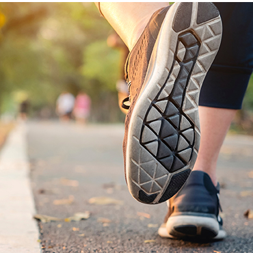 Close-up of a runner’s shoe stepping on a road at sunset, with a blurred park background