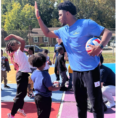 Teacher high-fiving children during an outdoor sports activity on a basketball court