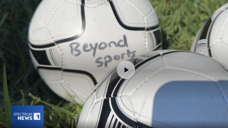 Soccer balls on grass, one marked “Beyond Sport,” with a news-style logo in the corner