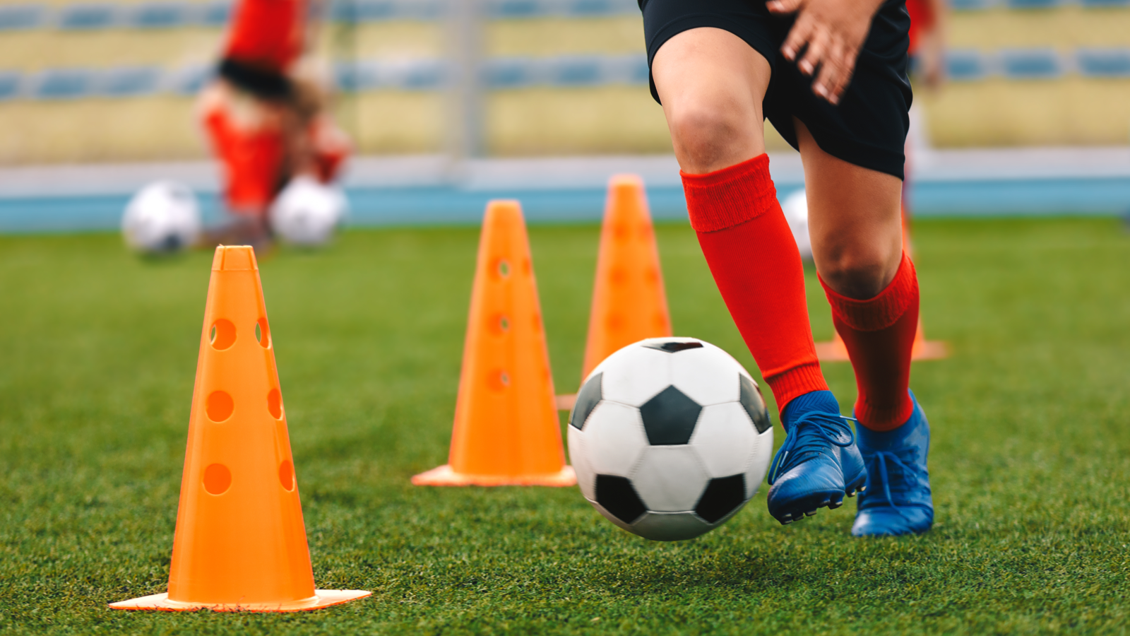 Child dribbling a soccer ball between orange training cones on a grassy field