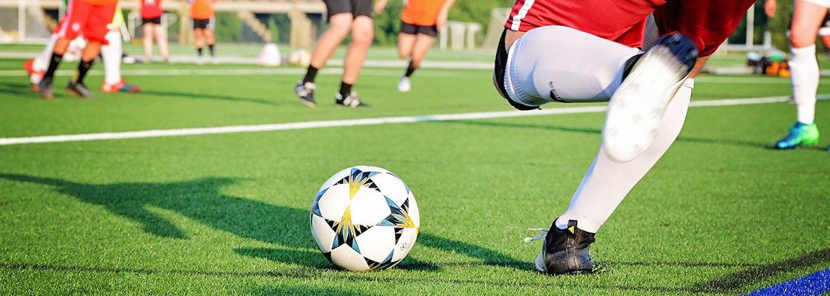Soccer player in red dribbles ball on green field with opponents in background