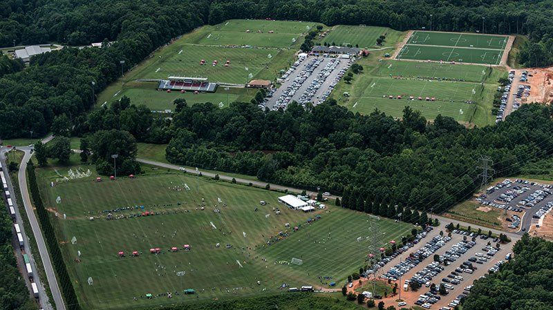 Aerial view of multiple green sports fields with parking lots and surrounding trees