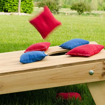 Outdoor lawn game with red and blue beanbags on a wooden board, one beanbag midair