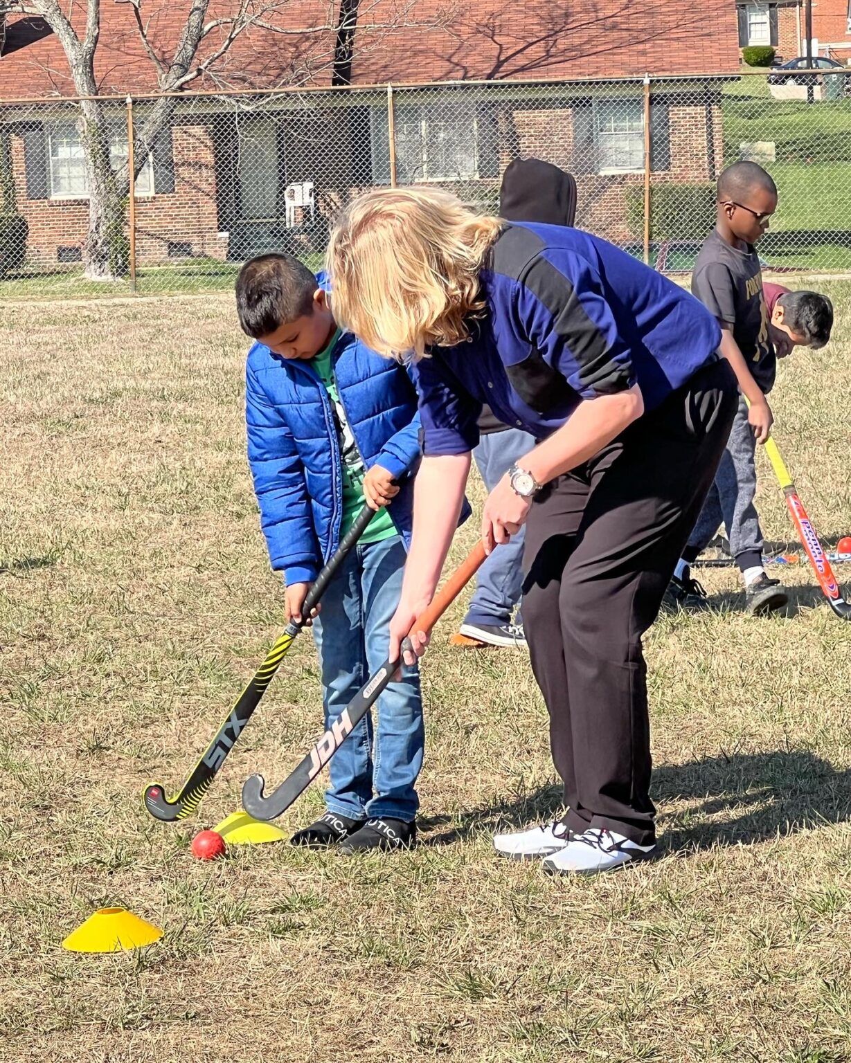 People playing mini-golf on a grassy field, with a woman helping a child line up a shot.