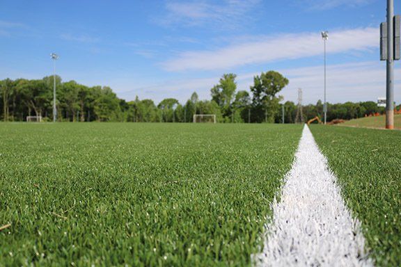 Soccer field with a white sideline, green turf, trees, and blue sky