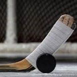A hockey stick balanced on a black puck on the ice, with a blurred rink background.