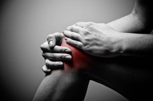 Hands clutching a bent knee with a red-highlighted area indicating knee pain.