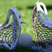 Two blue-and-white lacrosse sticks flanking a ball on grass