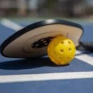 Yellow pickleball under a black-and-white paddle on a blue court surface