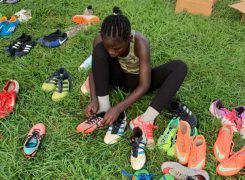 Person sitting on grass, tying shoes surrounded by colorful sneakers displayed around them.