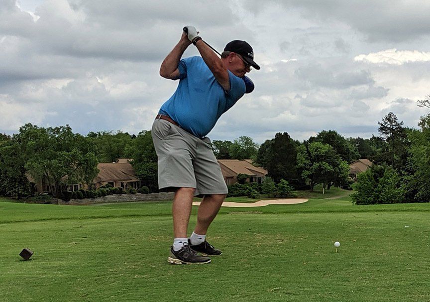 Golfer mid-swing on a green fairway under cloudy skies