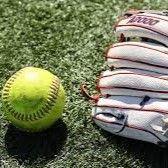 Softball and stacked white baseball gloves on green turf