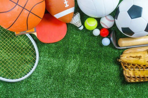 Assorted sports equipment on green turf, including balls, a tennis racket, and a baseball glove.