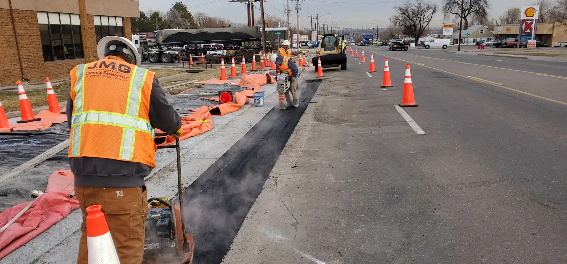 A traffic cone is sitting on the side of the road in the rain.