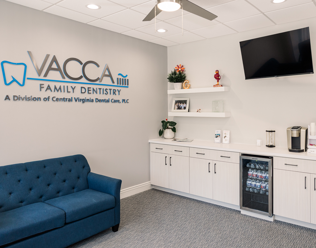 Dental office waiting room with blue couch, wall logo, white cabinets, TV, and coffee station