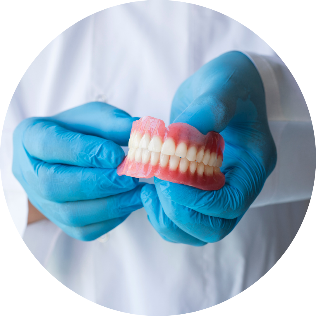 Blue-gloved hands holding a set of false teeth against a white coat background