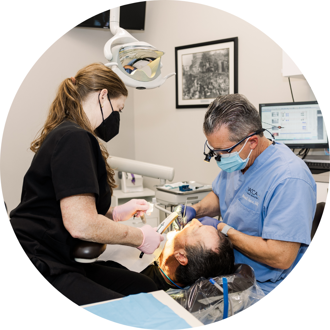 Dentist treating a patient while an assistant stands nearby in a dental clinic