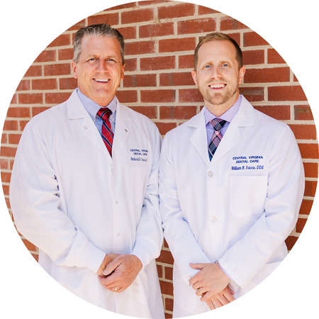 Two doctors in white coats standing in front of a brick wall, smiling at the camera.