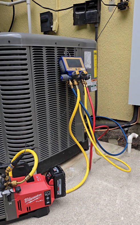 Outdoor air conditioner unit beside a house wall, with a fan grill and beige casing.