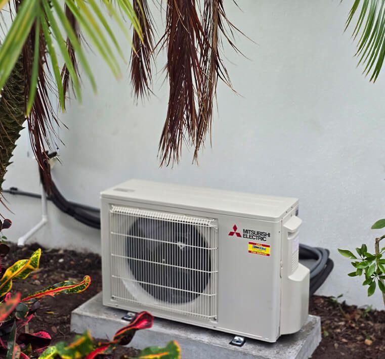 Outdoor air conditioner unit beside a house wall, with a fan grill and beige casing.