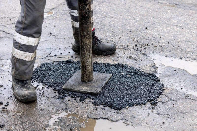 Person In Work Boots Compacting Asphalt In A Road Pothole — Hunter Valley Bitumen In Branxton, NSW