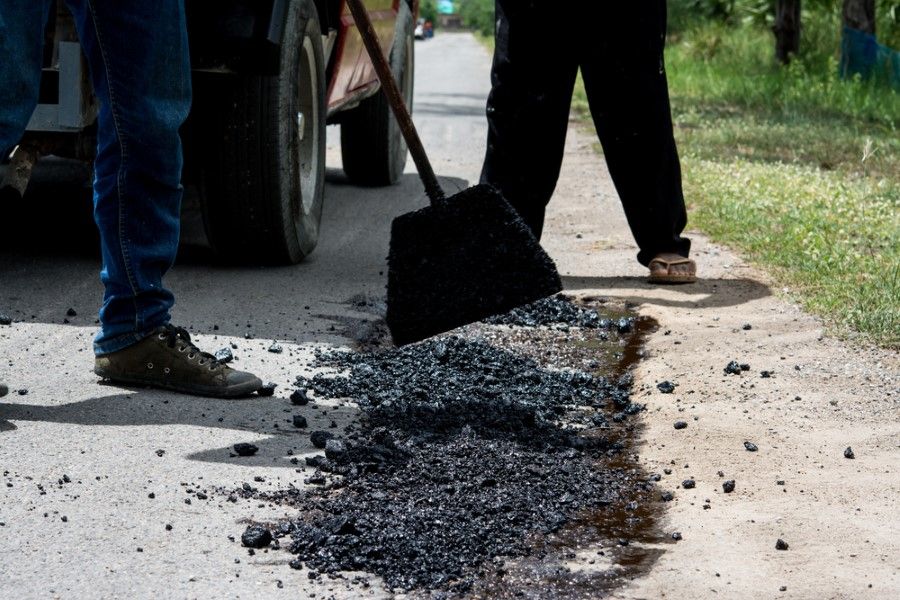 Road Workers Shovelling Asphalt Onto A Damaged Road Surface Next To A Truck — Hunter Valley Bitumen In Singleton, NSW