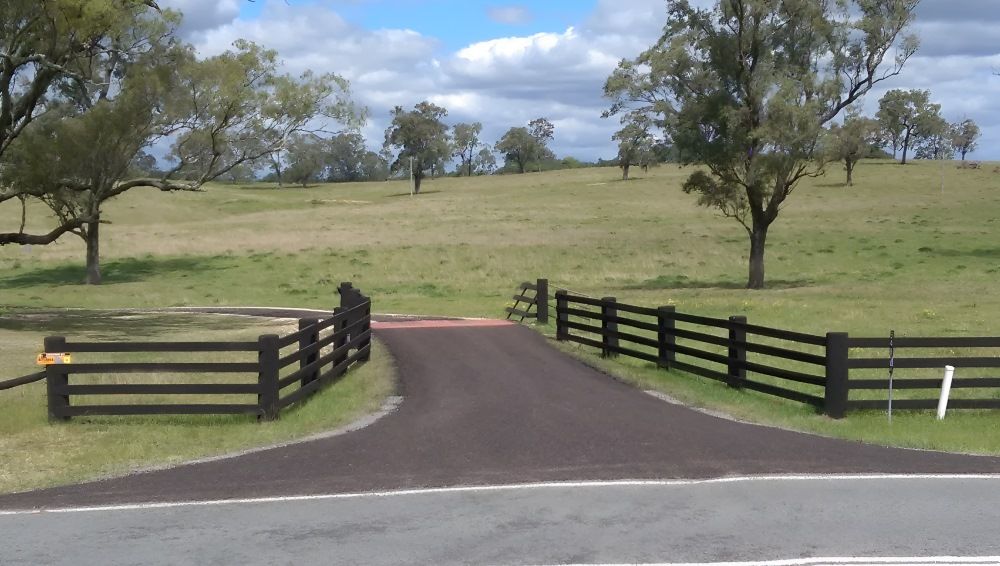 Newly paved driveway between black wooden fences leading into a grassy property. — Hunter Valley Bitumen In Maitland, NSW