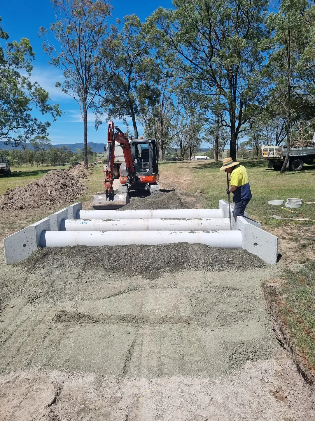 A Man Is Laying Large Pipes down on a driveway with a digger — Hunter Valley Bitumen In Maitland, NSW