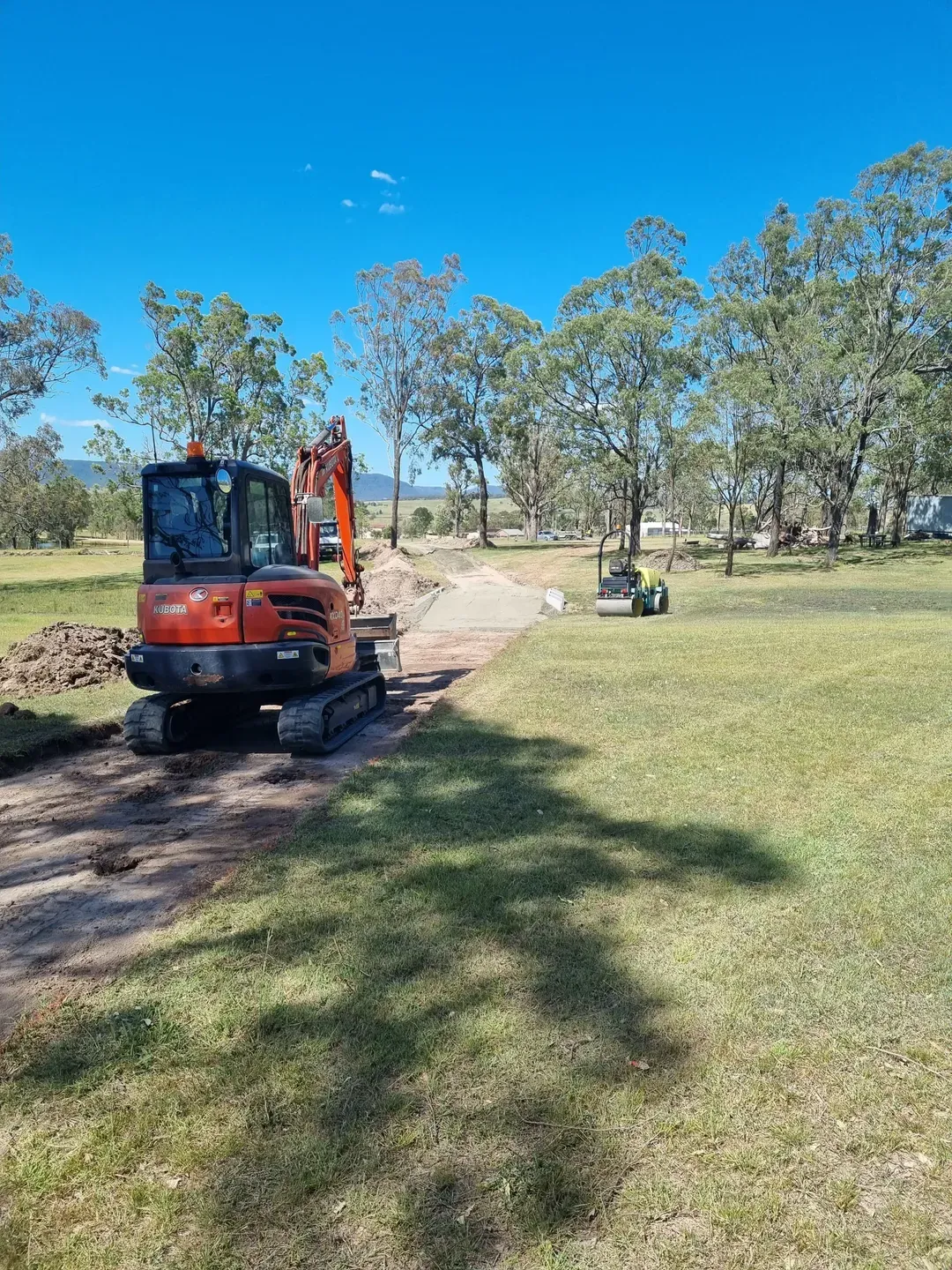 A Digger is on new driveway surrounded by trees— Hunter Valley Bitumen In Maitland, NSW