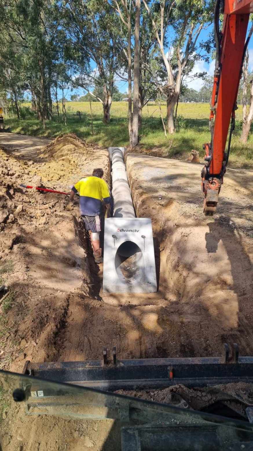 Worker and excavator installing concrete culvert pipe in trench – Hunter Valley Bitumen in Gresford, NSW.