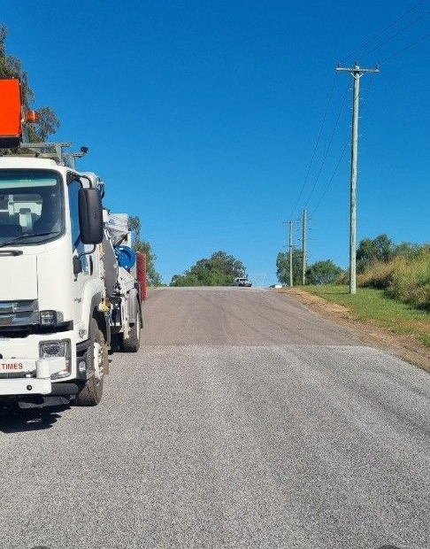 White truck parked on asphalt road under a clear blue sky, with power lines visible on a slight hill.