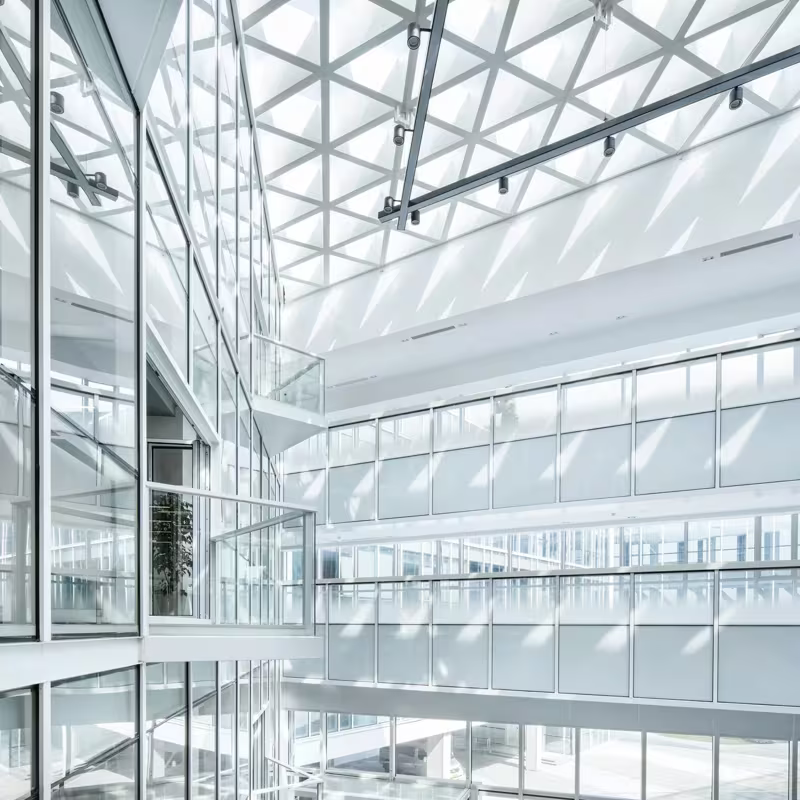Bright modern atrium with white glass walls, steel beams, and skylights flooding the interior with daylight