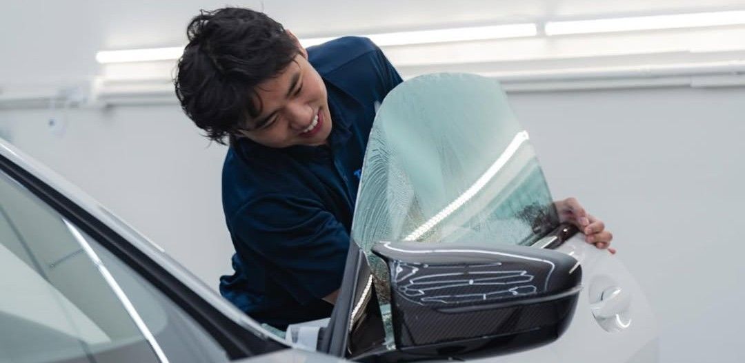 Person cleaning a car windshield with a cloth beside the side mirror