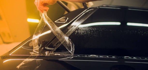 Person pouring water onto a glossy black car surface at a car wash